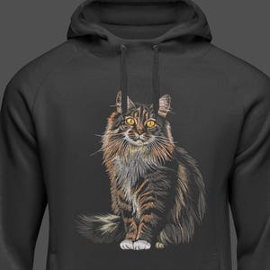 May include: A black hooded sweatshirt featuring a detailed illustration of a long-haired cat. The cat has brown, black, and white fur with yellow eyes. The cat is sitting upright, with its tail curled to the side.