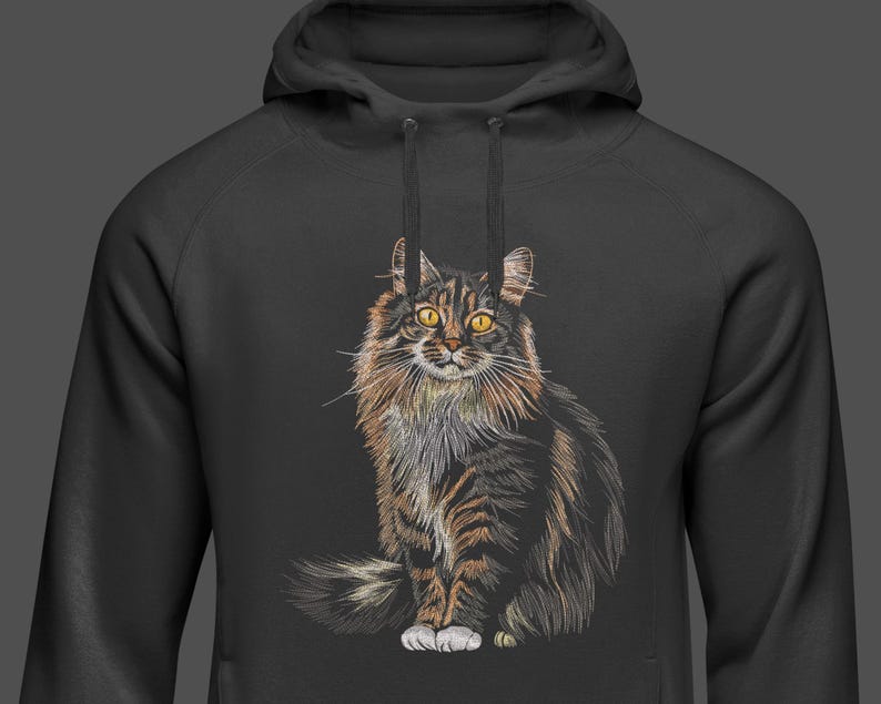 May include: A black hooded sweatshirt featuring a detailed illustration of a long-haired cat. The cat has brown, black, and white fur with yellow eyes. The cat is sitting upright, with its tail curled to the side.