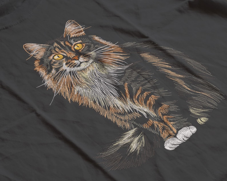 May include: Embroidered design of a long-haired cat with yellow eyes, brown and black fur, and white paws. The cat is lying down on a dark gray surface. The embroidery details the cat's fur and whiskers.