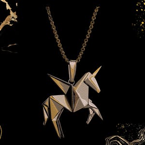 May include: A gold-toned metal pendant shaped like a geometric origami unicorn with wings, suspended from a matching gold-toned link chain. The pendant features sharp, angular facets that create a structured, multi-dimensional appearance.