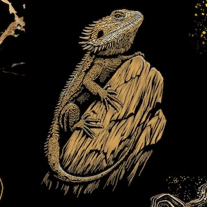Peut inclure: Illustration détaillée d'un lézard barbu aux tons or et marron, perché sur une surface en bois texturée. L'œuvre est posée sur un fond noir avec des éléments décoratifs dorés.