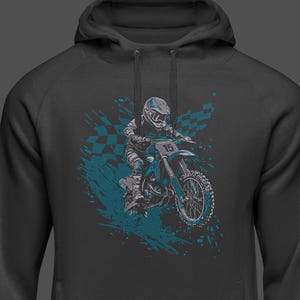 Puede incluir: Sudadera con capucha gris oscuro con un gr&aacute;fico turquesa y gris de un piloto de motocross en una moto azul. El dise&ntilde;o incluye una bandera a cuadros y un efecto de salpicaduras de pintura turquesa. El piloto lleva casco y el n&uacute;mero 15 es visible.