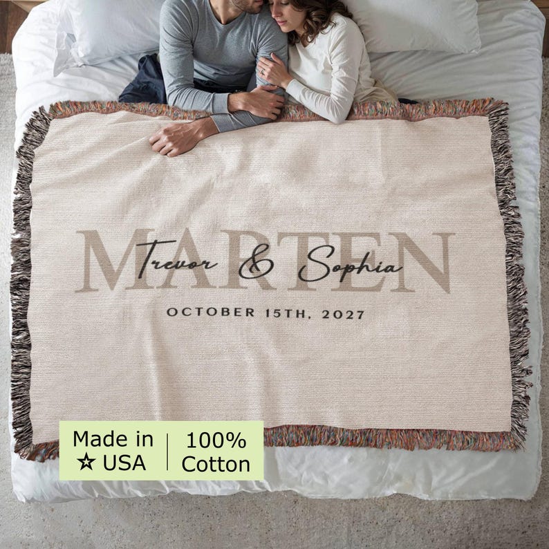 A couple cuddling on a bed with a blanket that says " Trevor & Sophia October 15th, 2027 Made in USA 100% Cotton".