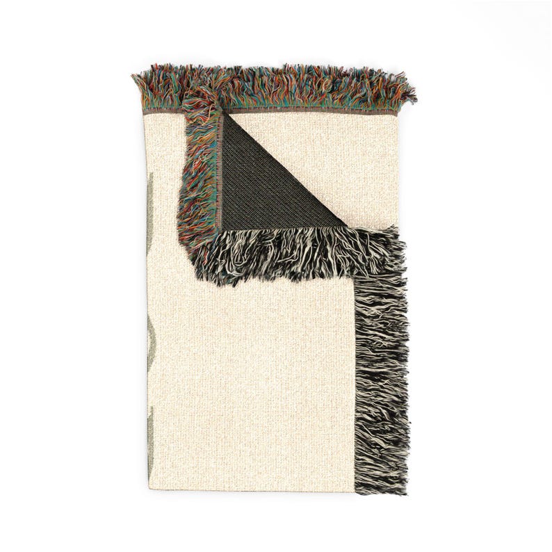 Woven blanket reverse side: A beige fabric with a black fringe on the edges, folded in half and displayed against a white background.