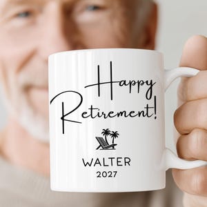 A person is holding a white mug with the text "Happy Retirement!" printed on it.