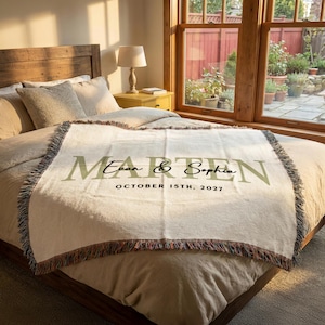 A bedroom with a large bed, a lamp, and a window overlooking a garden. The bed has a white blanket with the names "Ethan & Sophie" printed on it.