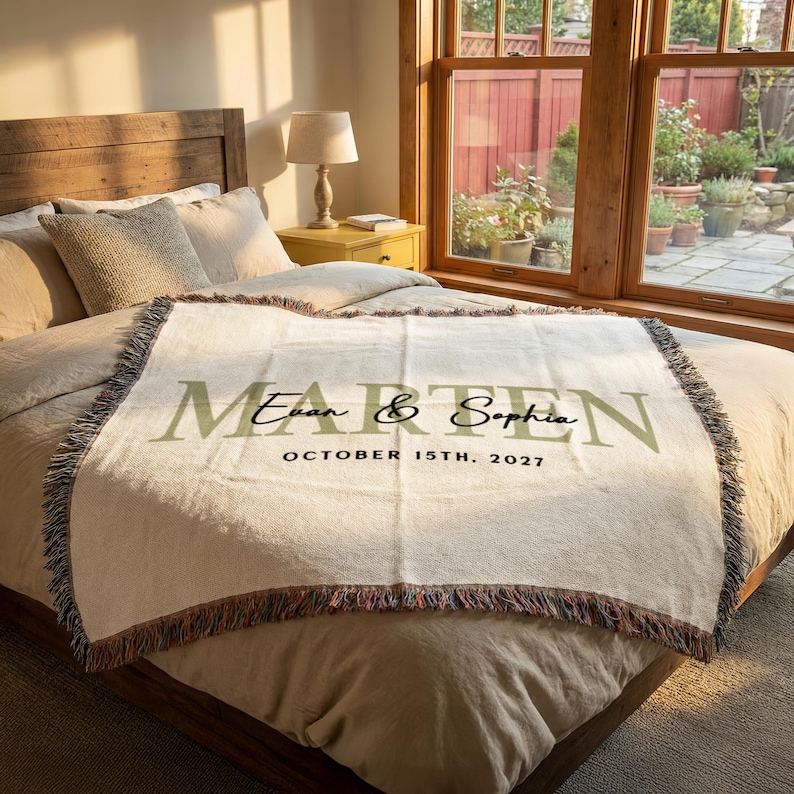 A bedroom with a large bed, a lamp, and a window overlooking a garden. The bed has a white blanket with the names "Ethan & Sophie" printed on it.