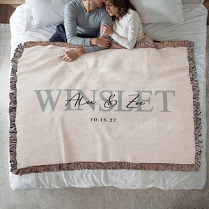 A couple lying on a bed, with a blanket that says "WINSLET" and the date "10.15.27" printed on it.