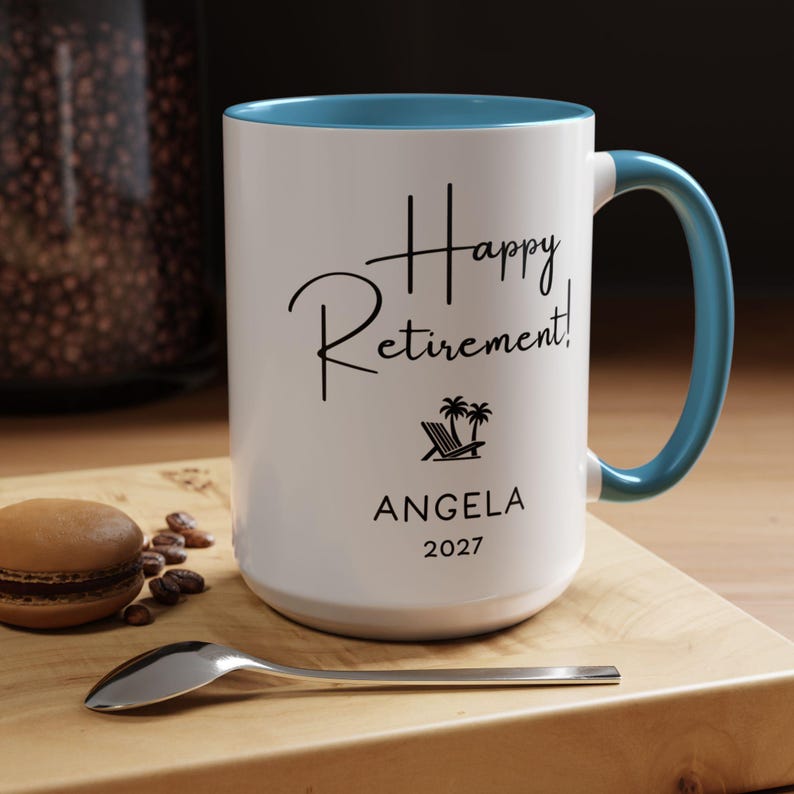 A white and blue mug with the text "Happy Retirement!" printed on it, placed on a wooden surface next to a spoon and some coffee beans.