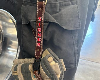 May include: A brown leather key chain with a metal clip and the word "SIGNER" embroidered in red.