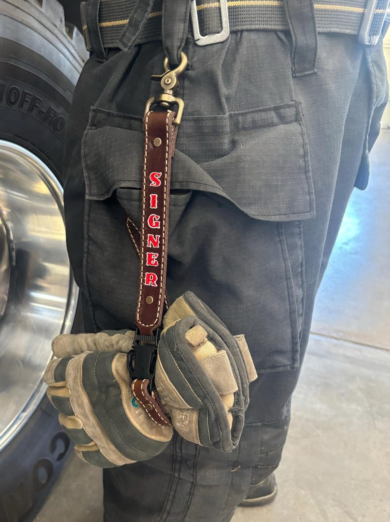 May include: A brown leather key chain with a metal clip and the word "SIGNER" embroidered in red.