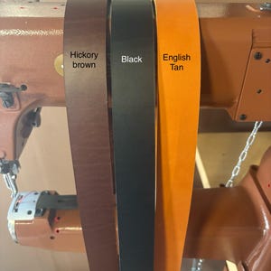 May include: Three leather straps in different colors: hickory brown, black, and English tan. The straps are on a sewing machine.