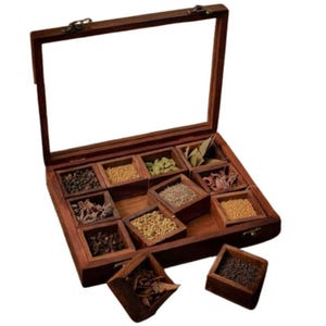 Puede incluir: Una caja de especias de madera con tapa de vidrio, que contiene ocho compartimentos llenos de diferentes especias. La caja est&aacute; hecha de madera marr&oacute;n oscura y tiene una tapa con bisagras. Los compartimentos est&aacute;n dispuestos en forma de cuadr&iacute;cula y est&aacute;n llenos de diferentes especias, incluyendo granos de pimienta negra, clavos, semillas de comino y semillas de cilantro.
