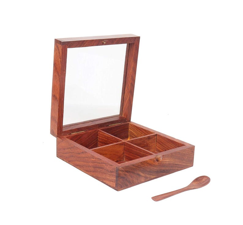Puede incluir: Una caja de madera con tapa de vidrio y cuatro compartimentos. La caja est&aacute; hecha de madera oscura con un tono rojizo. Se incluye una peque&ntilde;a cuchara de madera.