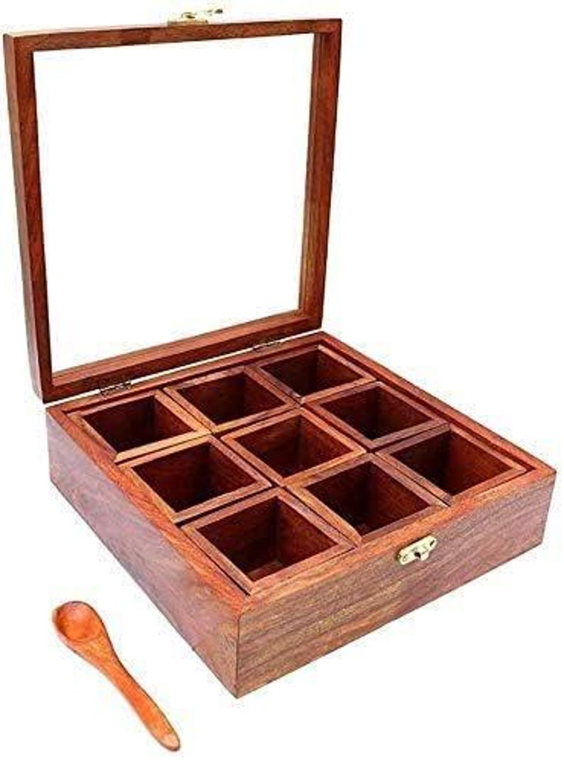 Puede incluir: Una caja de especias de madera con tapa de vidrio y ocho compartimentos. La caja est&aacute; hecha de madera oscura y tiene un cierre de lat&oacute;n. Se incluye una peque&ntilde;a cuchara de madera.