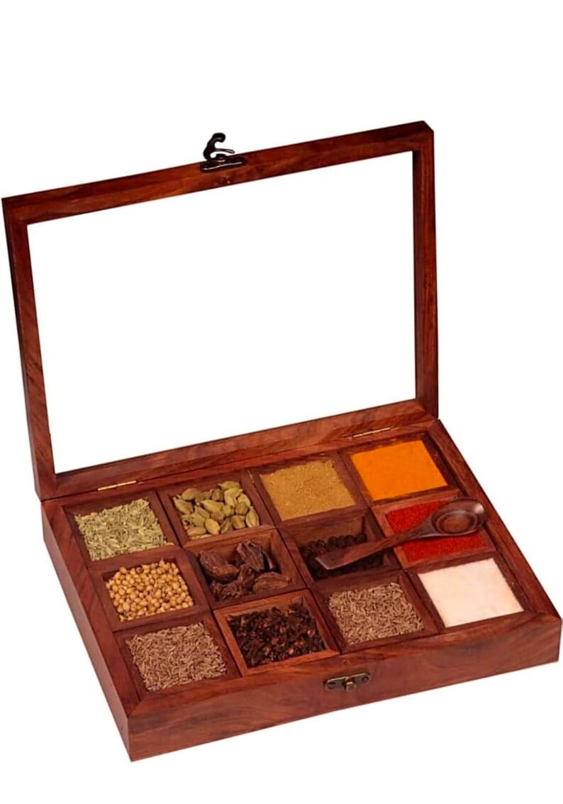 Puede incluir: Una caja de especias de madera con tapa de vidrio, dividida en nueve compartimentos. La caja est&aacute; llena de diversas especias, incluyendo comino, cilantro, c&uacute;rcuma y chile en polvo.