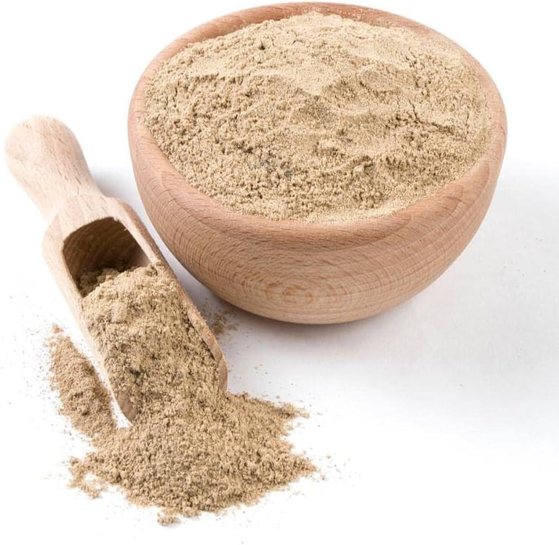 K&ouml;nnte beinhalten: Eine Holzsch&uuml;ssel und ein L&ouml;ffel gef&uuml;llt mit hellbraunem Pulver, wahrscheinlich ein Gew&uuml;rz oder Kraut. Die Sch&uuml;ssel ist rund und der L&ouml;ffel hat einen Griff. Das Pulver versch&uuml;ttet sich auf der wei&szlig;en Oberfl&auml;che und erzeugt eine nat&uuml;rliche und rustikale &Auml;sthetik.
