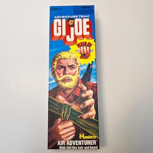 May include: A G.I. Joe Adventure Team Air Adventurer action figure box featuring a blonde bearded character illustration. The packaging includes the text Adventure Team, G.I. Joe, Kung Fu Grip, Hasbro, and Air Adventurer with life-like hair and beard.