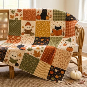 May include: A quilted throw blanket featuring a patchwork design with autumn-themed patterns, including black cats, ghosts reading books, pumpkins, and fall leaves in shades of orange, green, brown, and cream, draped over a wooden chair.