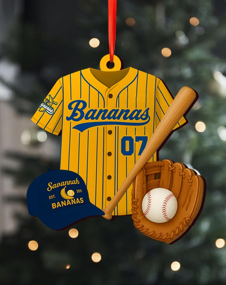 Pode incluir: Um enfeite com tema de beisebol com uma camisa amarela e azul com a palavra "Bananas" e o n&uacute;mero "07". Inclui um bast&atilde;o de beisebol, uma luva, uma bola e um bon&eacute; azul com o texto "Savannah Bananas". Uma fita vermelha est&aacute; presa.