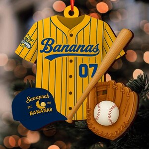 Pode incluir: Enfeite de Natal com tema de beisebol com camisa amarela e azul com "Bananas" e o n&uacute;mero "07", taco de beisebol, luva, bola e bon&eacute; azul com texto "Savannah Bananas". Para a &aacute;rvore de Natal.