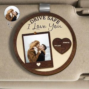 May include: A wooden car charm with a photo of a couple kissing, a heart-shaped puzzle with names, and the text "Drive Safe I Love You." The charm has a light wood center with a dark wood border and a metal clip for hanging.