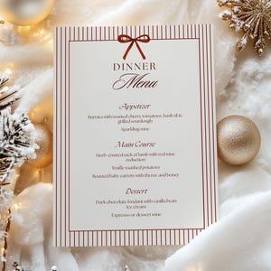 May include: A formal dinner menu with a burgundy bow and vertical stripes. The menu lists an appetizer, main course, and dessert. The menu is surrounded by Christmas ornaments and decorations.