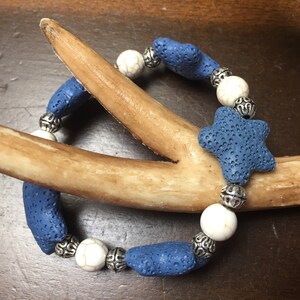 May include: A blue lava rock bracelet with white and silver beads. The bracelet features a star-shaped lava rock bead.