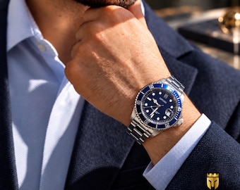 Può includere: Un orologio da polso in acciaio inossidabile con una lunetta girevole blu e un quadrante blu scuro con la scritta DIVODI. L'orologio presenta un cinturino a maglie in metallo color argento, indici luminosi e una finestrella della data a ore tre.