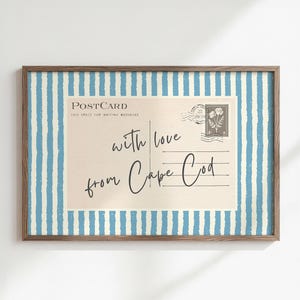 Peut inclure: Une impression murale rectangulaire dans un cadre en bois foncé présentant un design de carte postale vintage avec le texte 'with love from Cape Cod' en écriture noire, sur un fond de rayures verticales bleu clair et blanches.