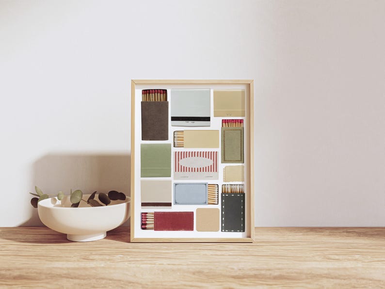 May include: A framed collage of matchboxes with various colors and patterns, including red, white, blue, green, and brown. The matchboxes are arranged in a grid pattern and are displayed against a white background.
