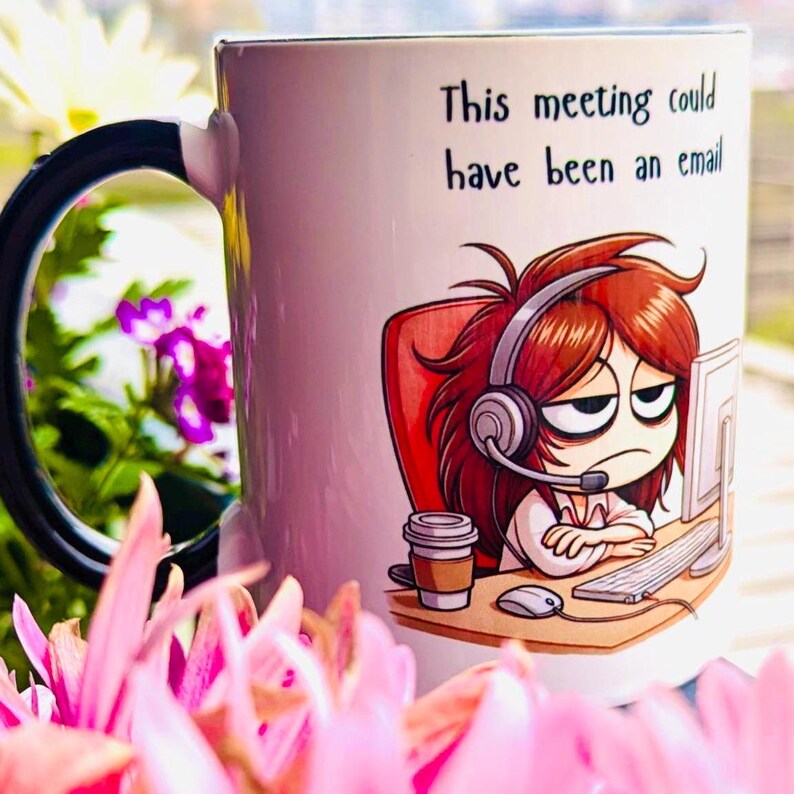 May include: White ceramic mug with a black handle. The mug features a cartoon illustration of a woman wearing a headset and sitting at a computer. The text "This meeting could have been an email" is printed on the mug.