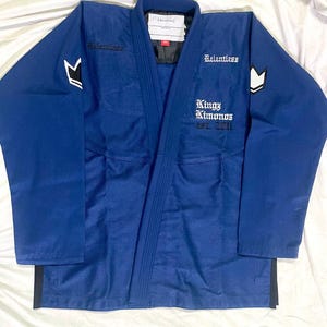 Può includere: Un gi da arti marziali blu navy con la scritta "Relentless" e "Kingz Kimonos Est. 2011". Il gi presenta dettagli bianchi e neri sulle maniche e sul colletto. Il gi è realizzato in un tessuto resistente.