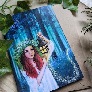 Puede incluir: Una mujer con el pelo largo y rojo y una corona de flores sostiene una linterna en un entorno de bosque oscuro. La linterna está encendida y proyecta un brillo cálido. La mujer lleva un vestido blanco y está rodeada de flores azules.