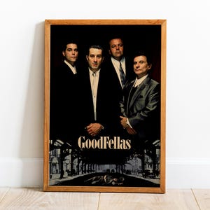 Puede incluir: Un póster enmarcado de la película "Goodfellas". La imagen muestra a cuatro hombres con trajes sobre un fondo oscuro. El título "Goodfellas" se muestra en una fuente estilizada en la parte inferior, con una escena callejera en blanco y negro.