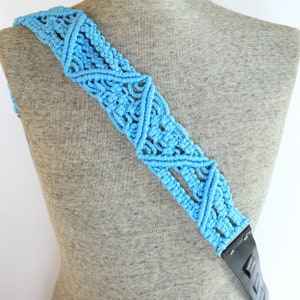 May include: A light blue crocheted guitar strap with a black leather end. The strap is made with a repeating triangle pattern.