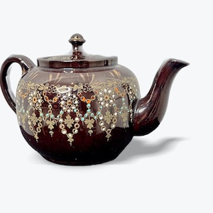 May include: A dark brown ceramic teapot with a lid and handle. The teapot is decorated with gold, white, turquoise, and orange floral patterns. The spout and handle are curved.