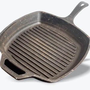 Może przedstawiać: Kwadratowa patelnia grillowa z żeliwa z uchwytem. Patelnia ma podniesione żebra na powierzchni do gotowania. Patelnia jest ciemnoszara i wydaje się dobrze doprawiona. Uchwyt jest przymocowany do boku patelni. Patelnia jest przeznaczona do grillowania.