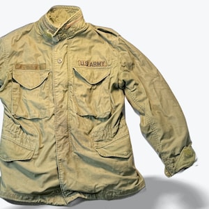 May include: An olive green military jacket featuring multiple front pockets, a button closure, and the text "US ARMY" on the chest. The jacket has a high collar and adjustable cuffs. A classic military garment.