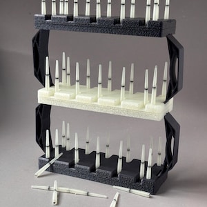 May include: Three-tiered black and white plastic laboratory equipment. Each tier holds multiple white, conical, and cylindrical items. Several of the white items are scattered in front of the equipment. The equipment has black handles on the sides.