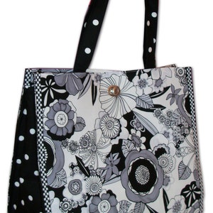 Pode incluir: Uma bolsa tote preta e branca com estampa floral. A bolsa tem uma al&ccedil;a de bolinhas pretas e brancas e uma borda xadrez preta e branca.