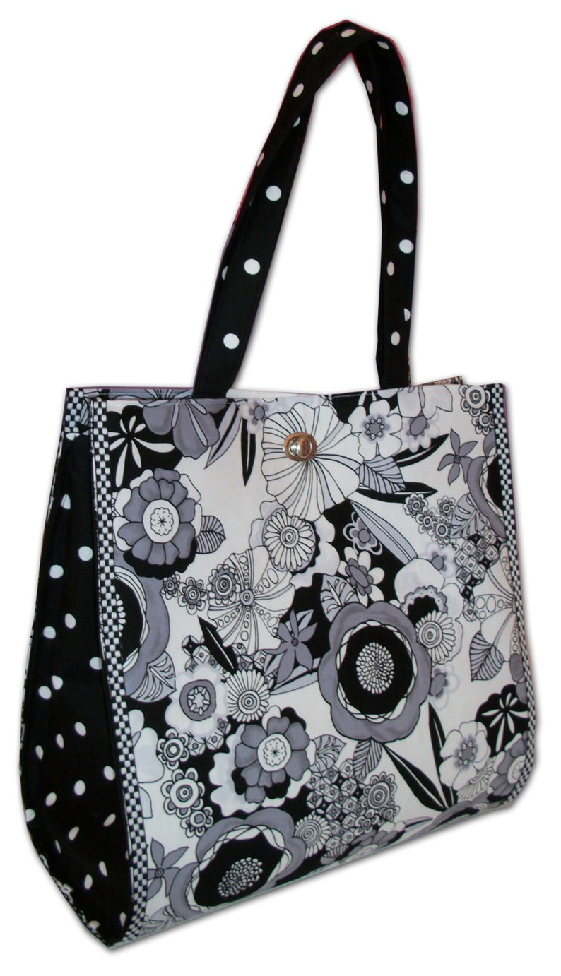 Pode incluir: Uma bolsa tote preta e branca com estampa floral. A bolsa tem uma al&ccedil;a de bolinhas pretas e brancas e uma borda xadrez preta e branca.
