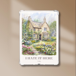 Peut inclure: Une coque de téléphone transparente rectangulaire présentant une illustration à l'aquarelle d'un cottage en pierre entouré d'un jardin vibrant avec des tulipes roses et des fleurs jaunes. Le texte I HATE IT HERE et TTPD est imprimé en bas.