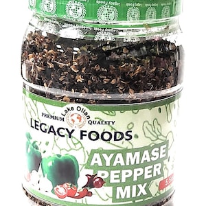 May include: A clear glass jar filled with Ayamase Pepper Mix. The jar has a green lid and a label with the text "Legacy Foods" and "Ayamase Pepper Mix". The label also features illustrations of green peppers, tomatoes, and garlic.