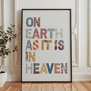 May include: A framed art print with the words "ON EARTH AS IT IS IN HEAVEN" in colorful patchwork letters. The letters are made from various patterned fabrics, set against a white background, and framed in black.