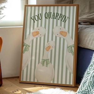Könnte beinhalten: Gerahmter Kunstdruck mit drei weißen Gänsen mit orangefarbenen Schnäbeln und grünen Schleifen, vor einem grün-weiß gestreiften Hintergrund. Die Worte "YOU QUAPPIN'" sind oben aufgedruckt. Das Kunstwerk befindet sich in einem Holzrahmen.