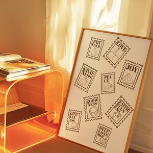 May include: A framed print featuring postage stamp designs with words like "Love," "Joy," and "Patience," each accompanied by a related illustration. The print is displayed in a room with a modern, orange-tinted side table and a sheer curtain.