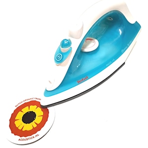 Op de afbeelding: Een wit en blauw Tefal strijkijzer met een ronde draaiknop en een knop op het handvat. Het strijkijzer ligt op een ronde, kleurrijke sticker met de tekst "Dutch Organic Train" en "acoustick.nl".