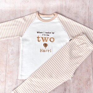 May include: White and beige striped pyjamas with a white long-sleeved top that says "When I wake up I'll be two" with a hot air balloon graphic and the name "Harri".