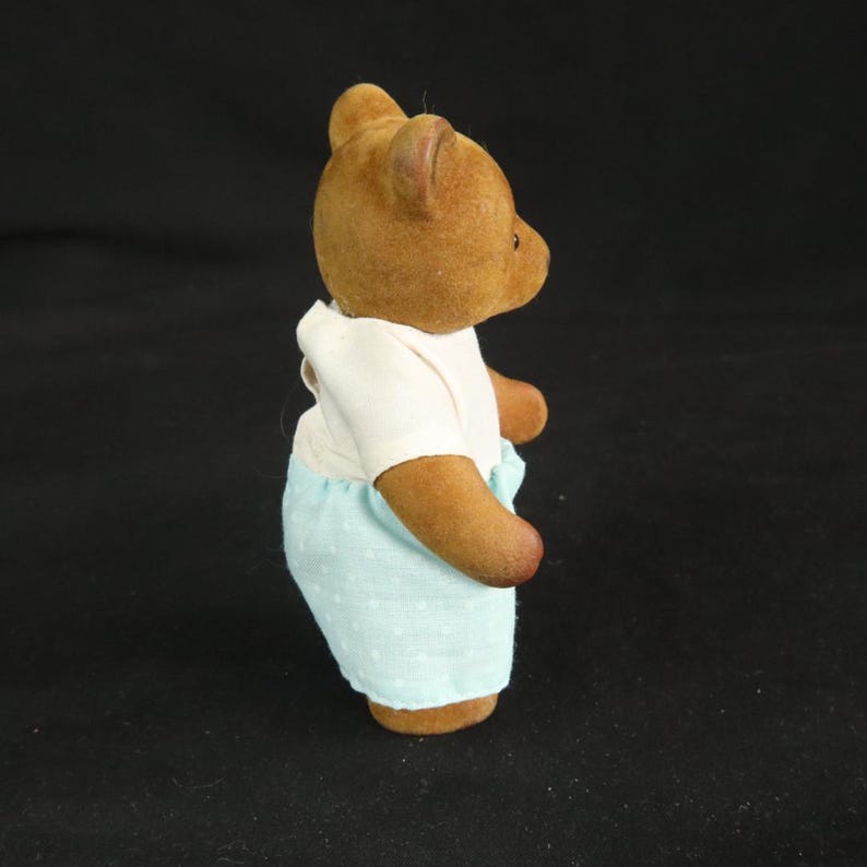 Peut inclure: Une petite figurine d'ours brun floqu&eacute; vue de profil. L'ours porte un haut blanc &agrave; manches courtes et un pantalon bleu clair avec un motif discret de pois blancs. La figurine pr&eacute;sente des oreilles arrondies et une texture douce et velout&eacute;e.